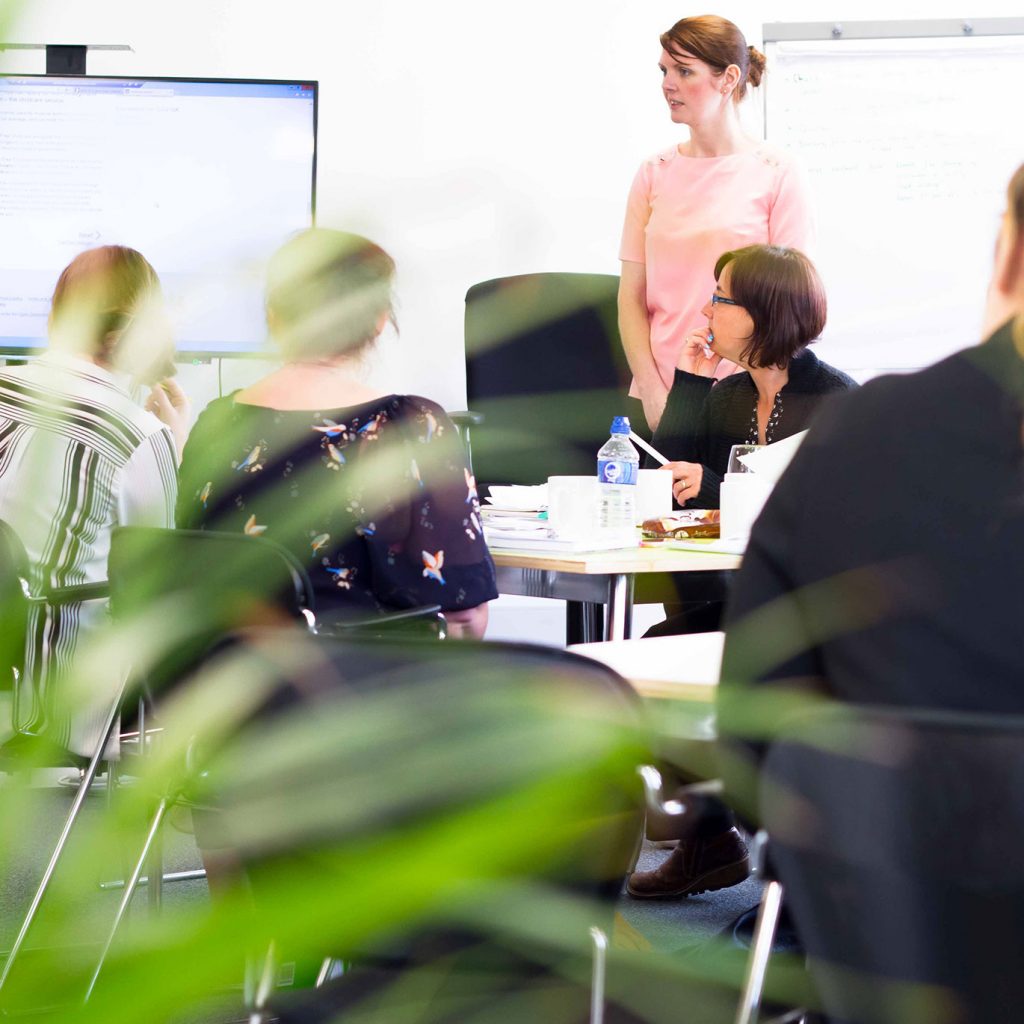 People sat around conference table looking at presentation screen