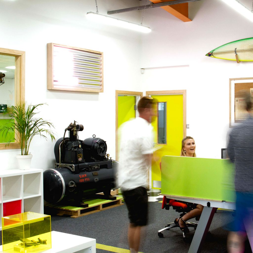 Members talking around coworking desks with old compressor in background