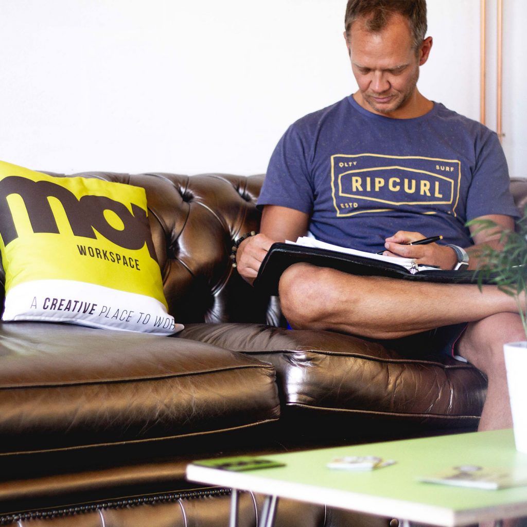 Member sat on sofa alongside branded Mor cushion and reading book